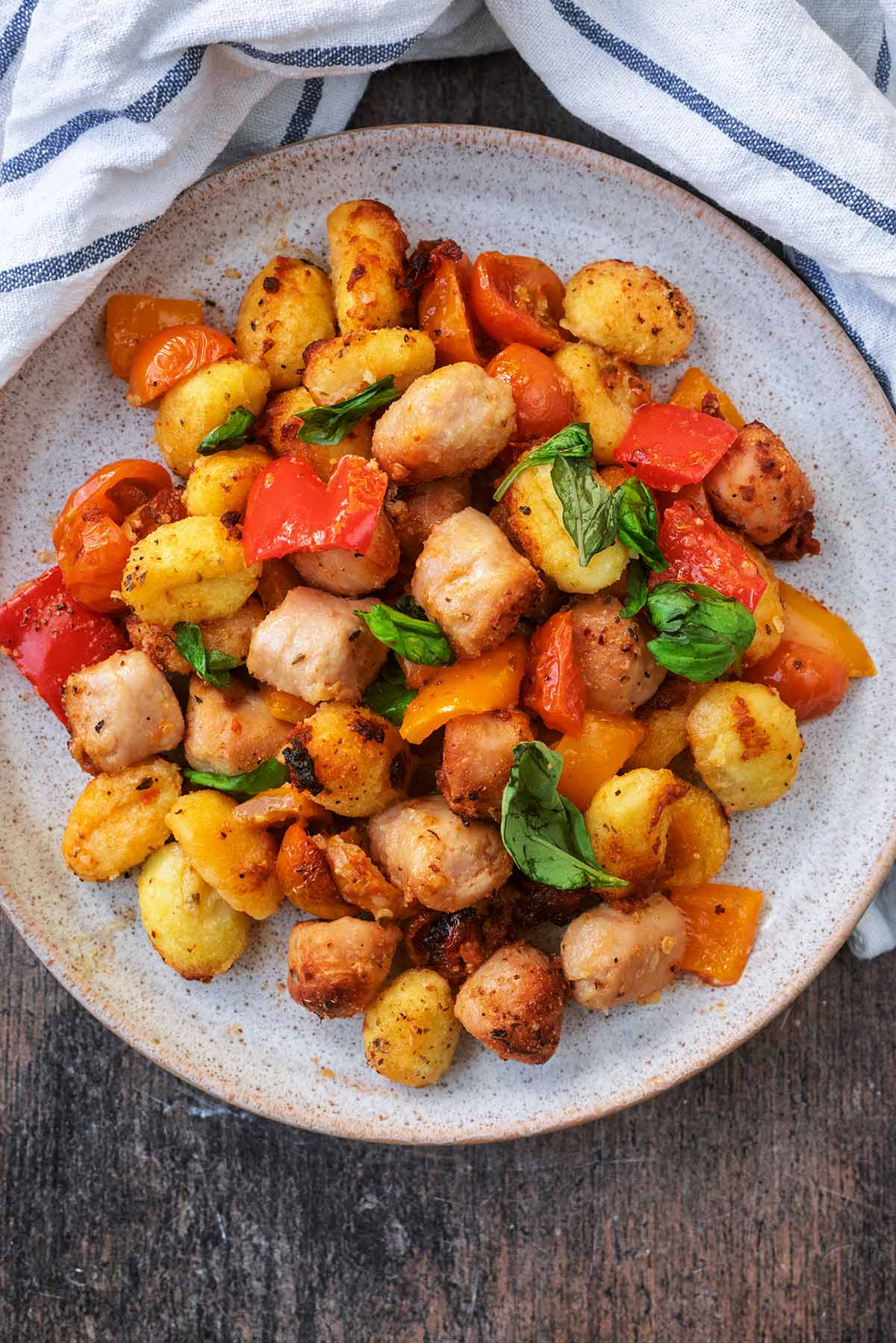 A round grey plate with cooked sausage chunks, gnocchi and vegetables.