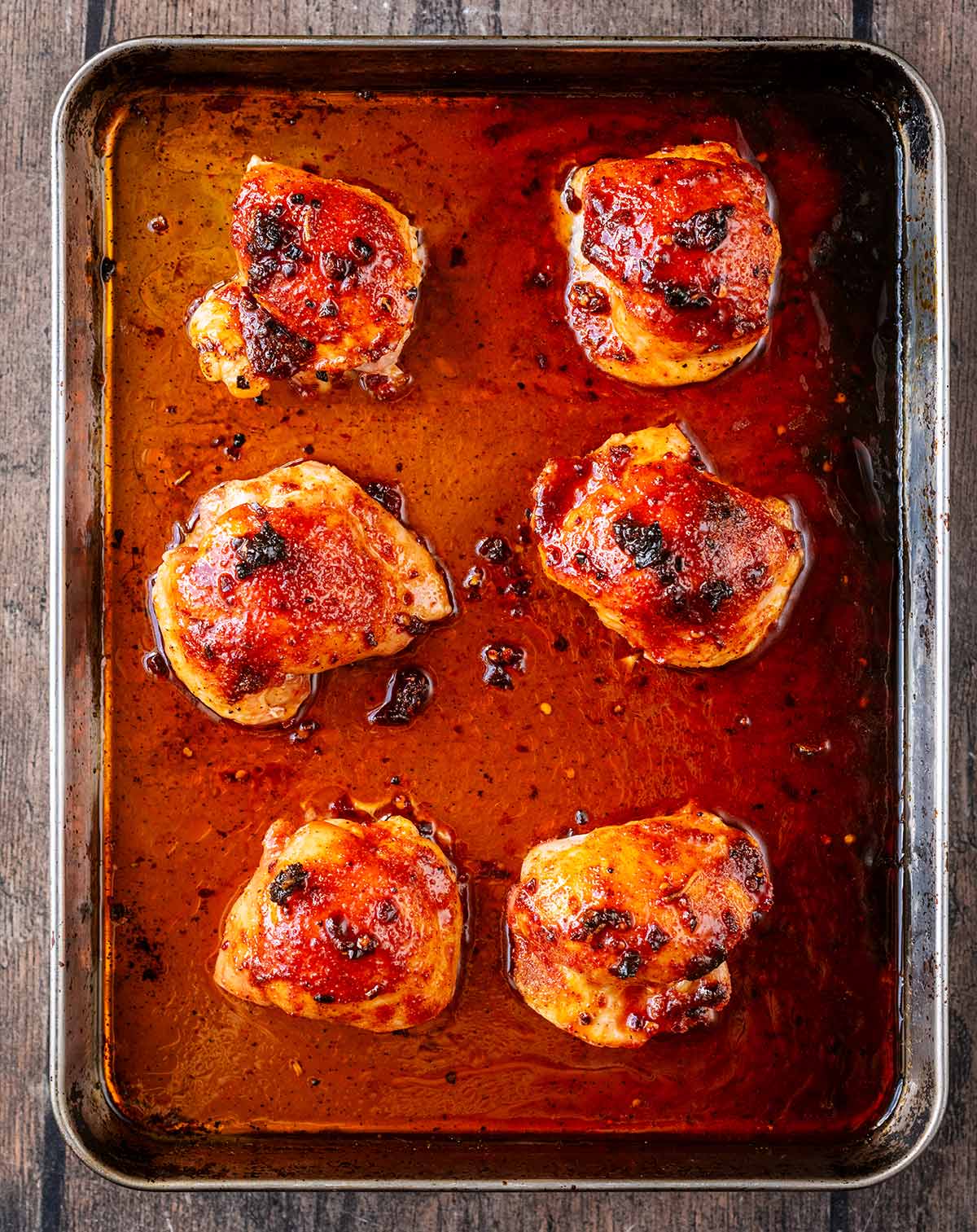 The cooked chicken thighs on the tray coated in the honey sauce.
