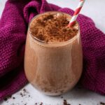 Chocolate protein shake in a glass with a red and white striped straw.