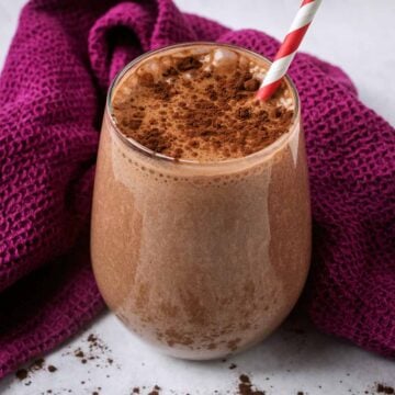 Chocolate protein shake in a glass with a red and white striped straw.