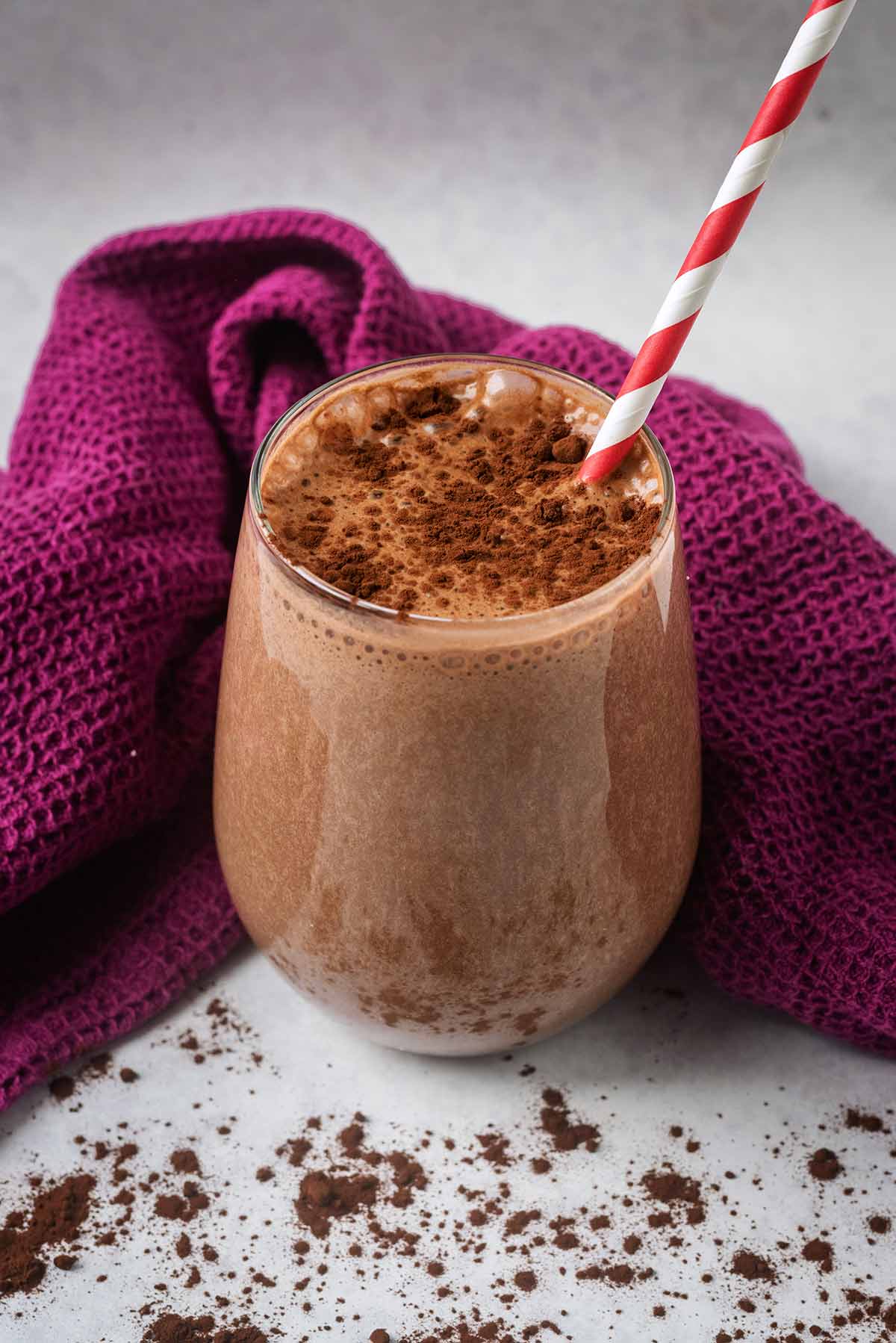 A chocolate milkshake in a glass in front of a purple towel.