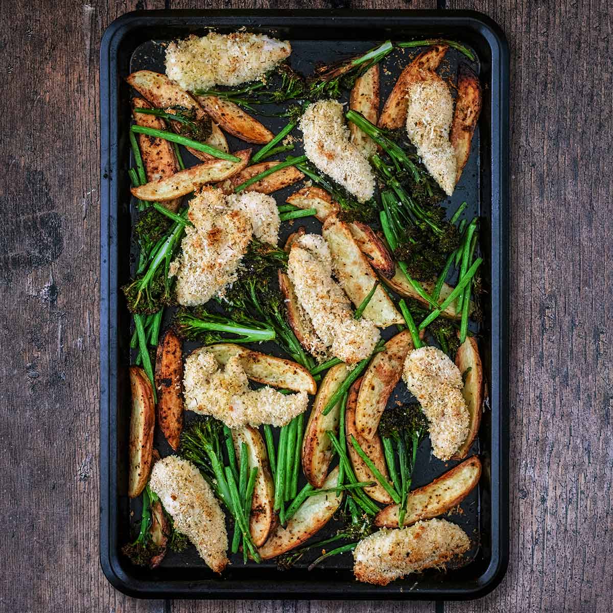 Crispy parmesan chicken traybake on a wooden surface.