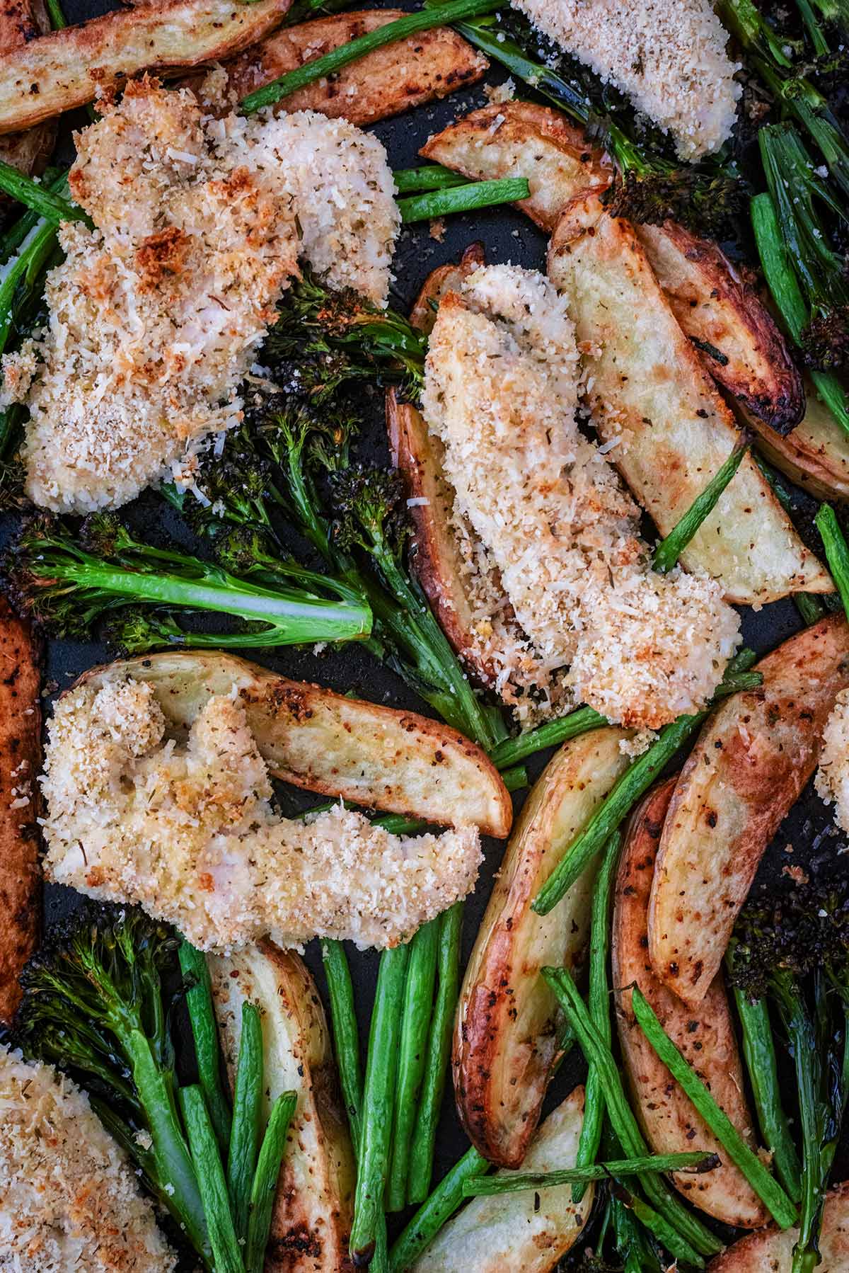 Crispy chicken tenders, golden potato wedges, broccoli and green beans all on a baking tray.