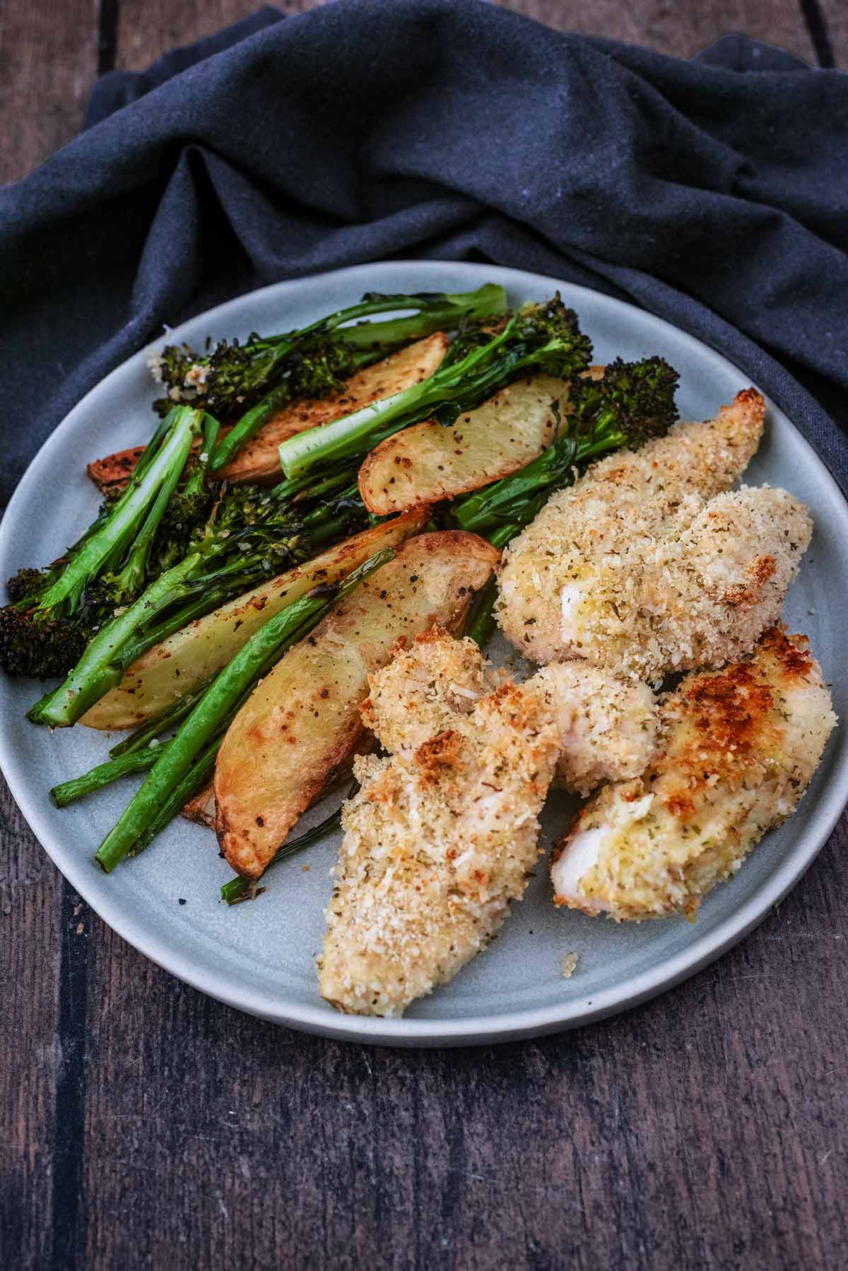A plate with coated chicken tenders, potato wedges, and vegetables.