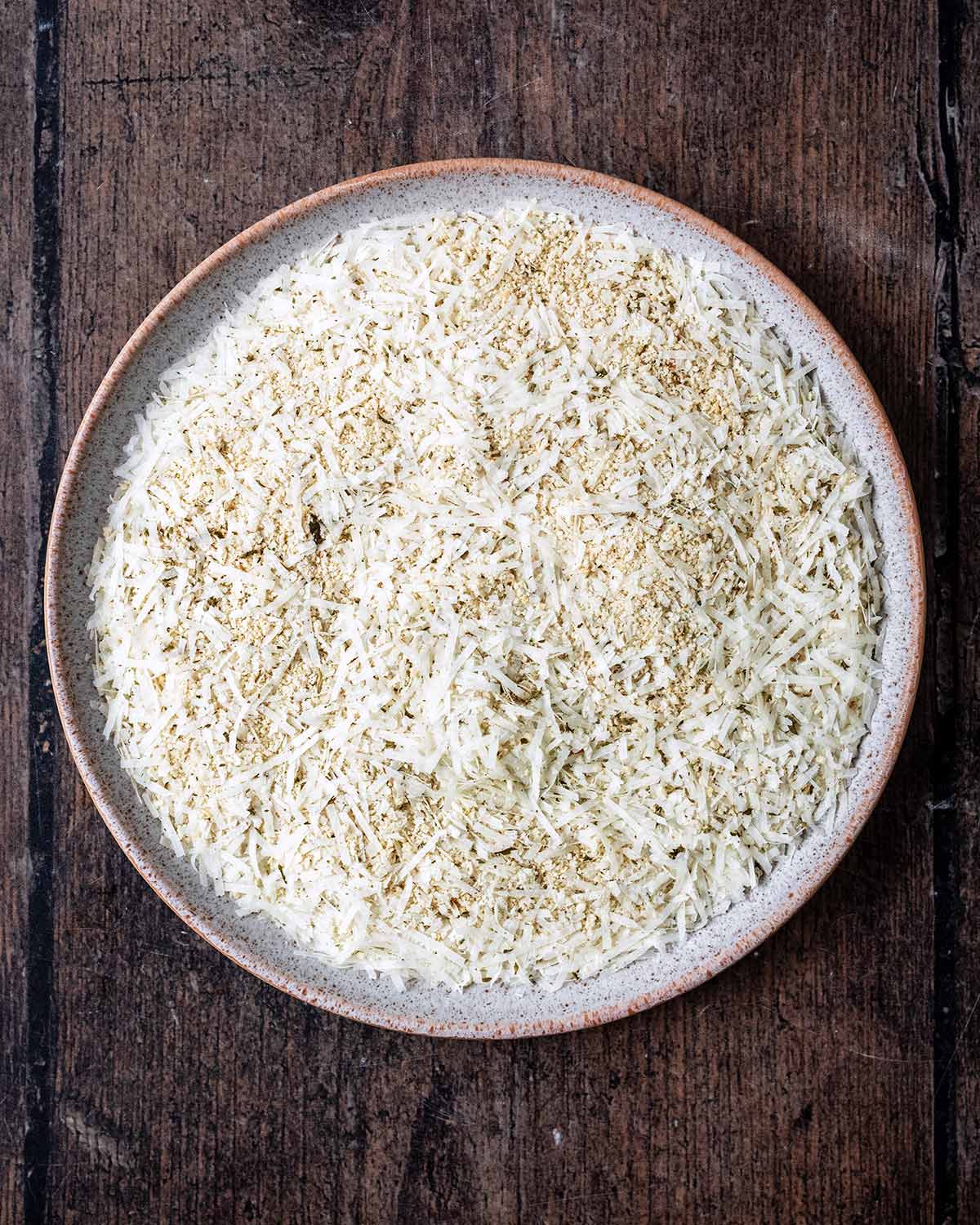 A plate of breadcrumbs, grated parmesan cheese and herbs all mixed together.