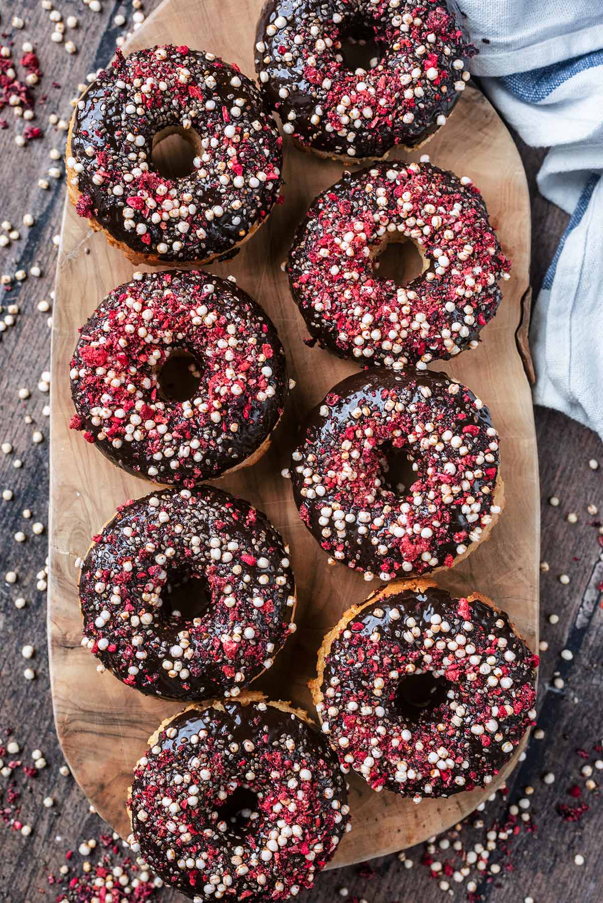 Eight chocolate topped ring donuts on a wooden serving board.