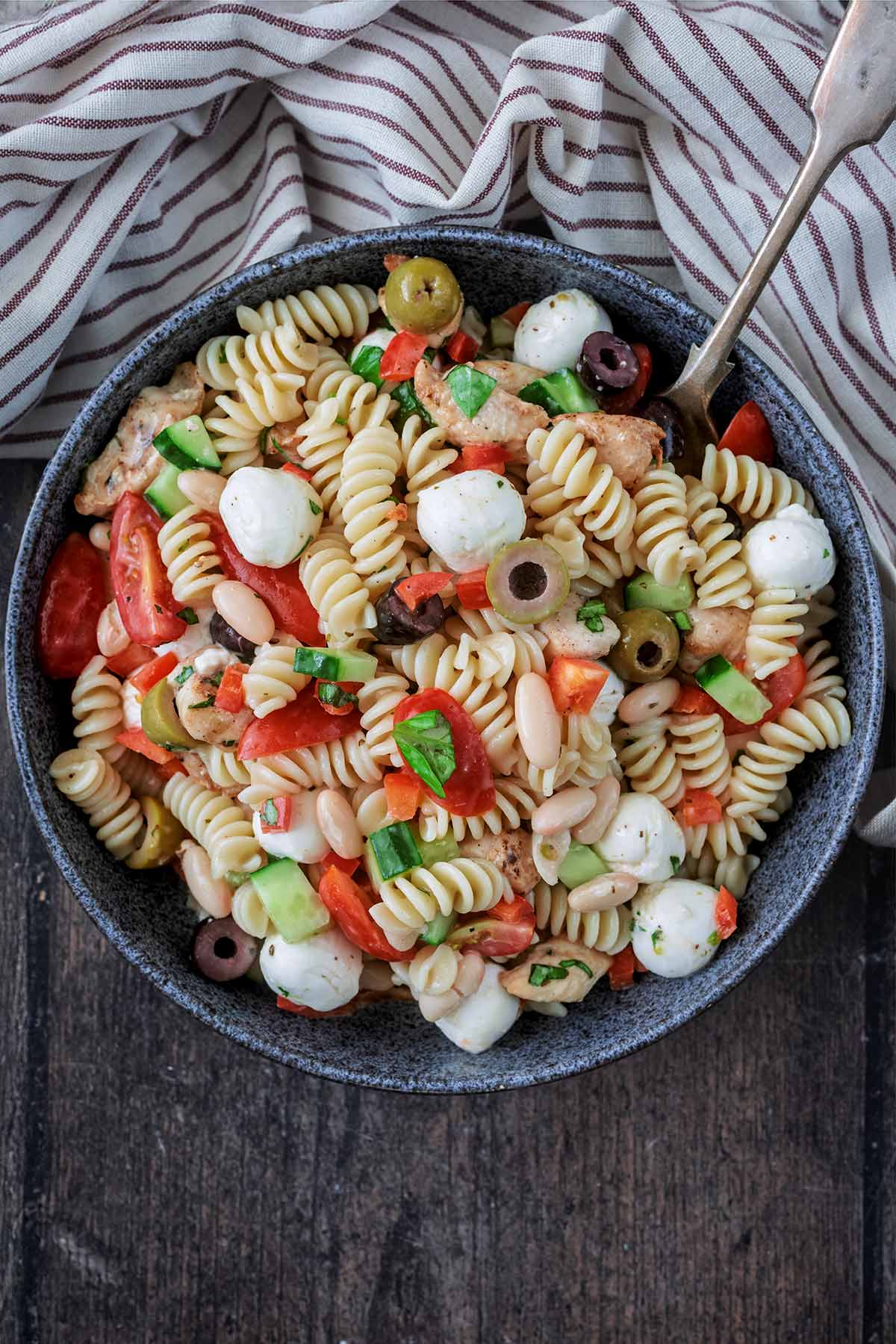A bowl of pasta salad next to a striped towel.