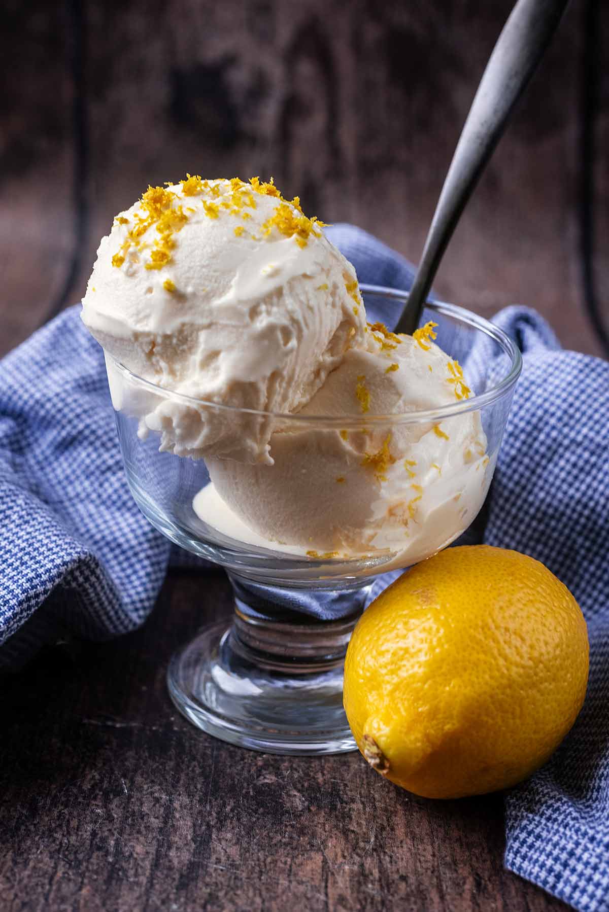Two balls of lemon ice cream in a serving class next to a whole lemon.