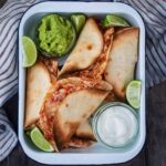 A serving tin containing oven baked chicken tacos, guacamole and sour cream.