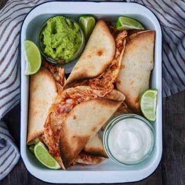 A serving tin containing oven baked chicken tacos, guacamole and sour cream.