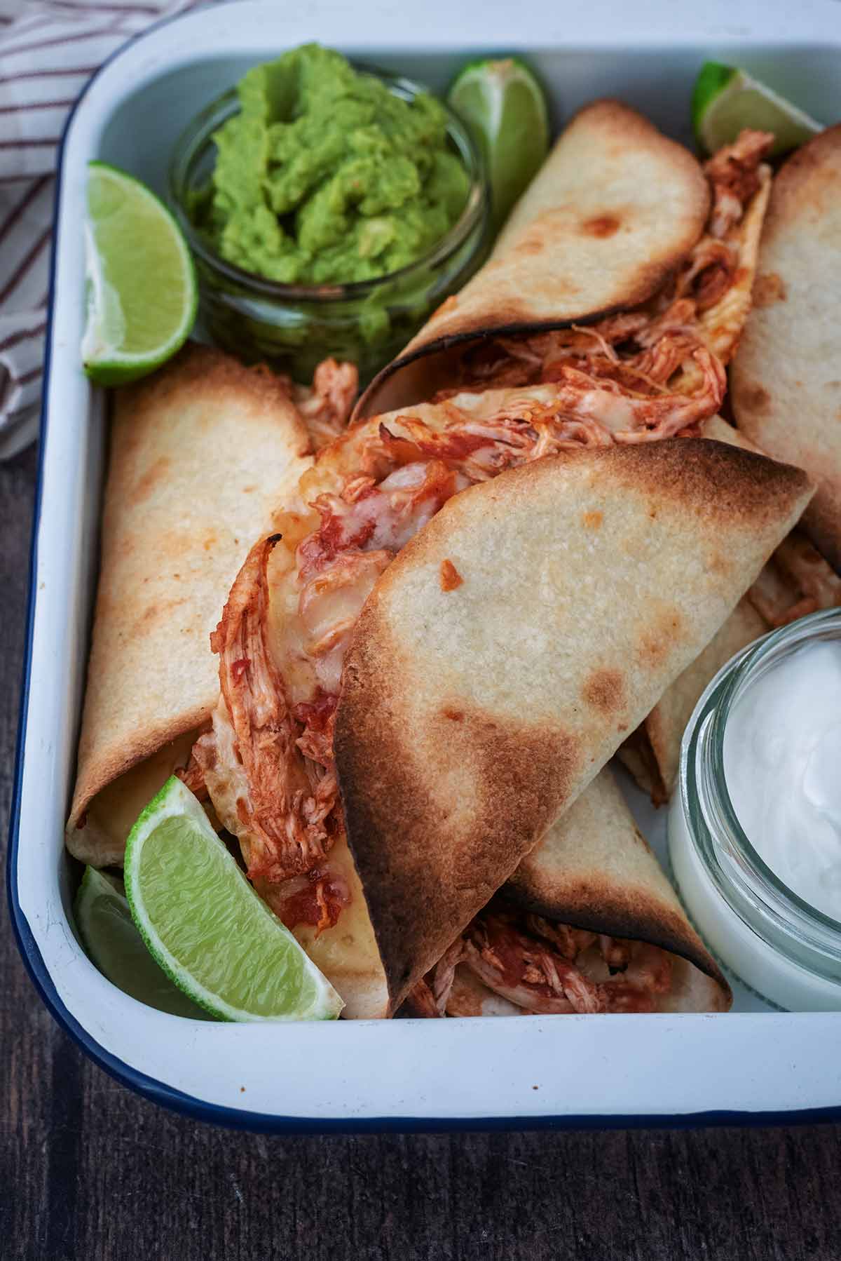 A tray of chicken tacos with guacamole and lime wedges.