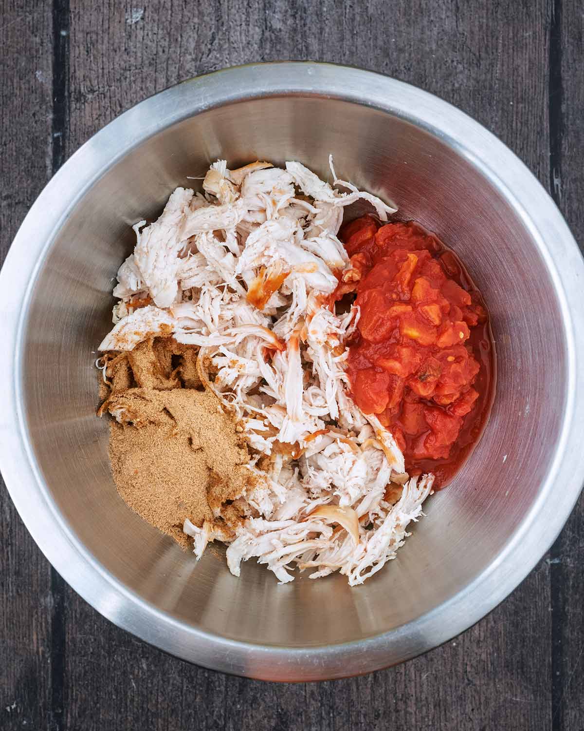 Shredded cooked chicken, chopped tomatoes and seasoning in a mixing bowl.