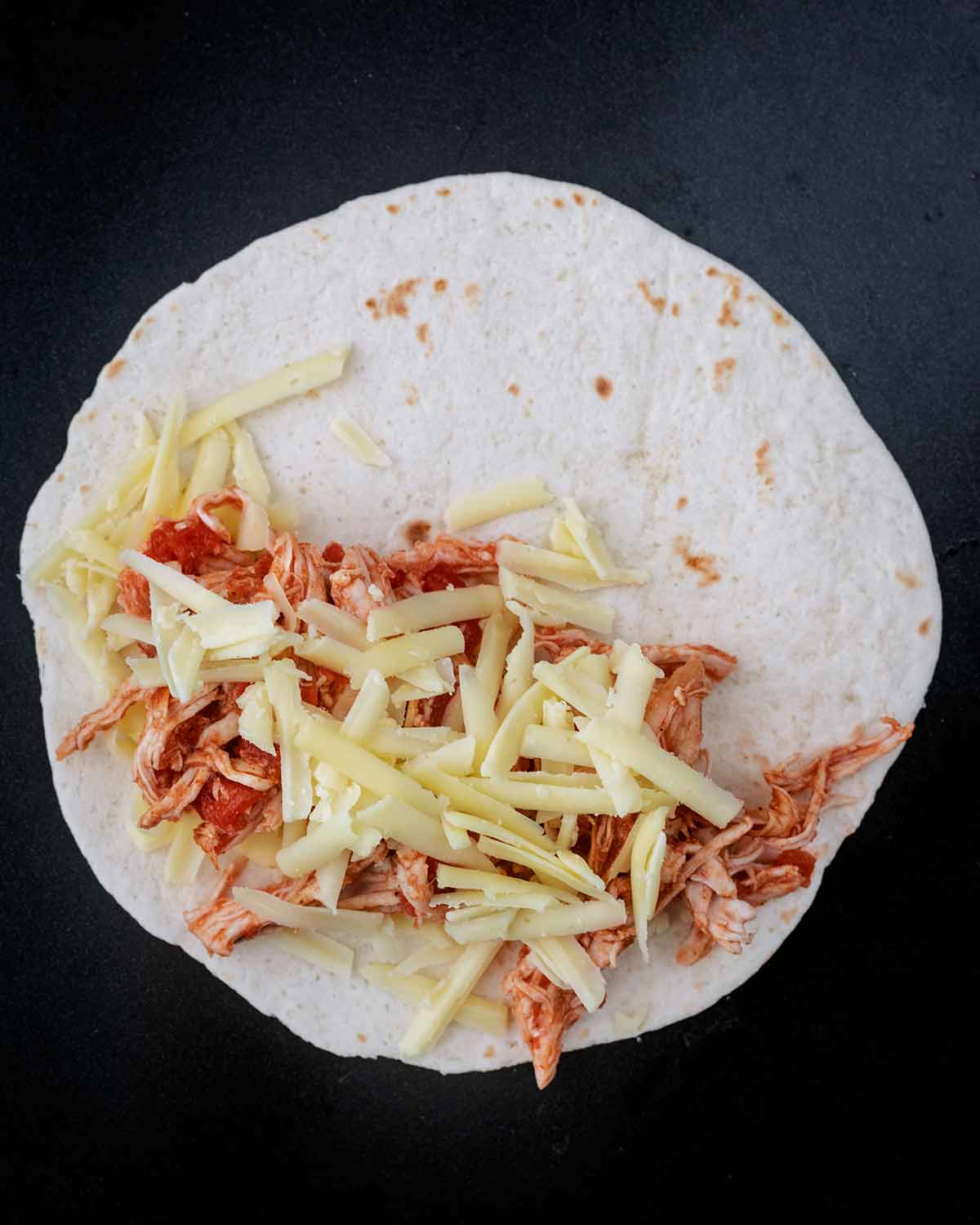 A flour tortilla, half topped with shredded chicken and grated cheese.