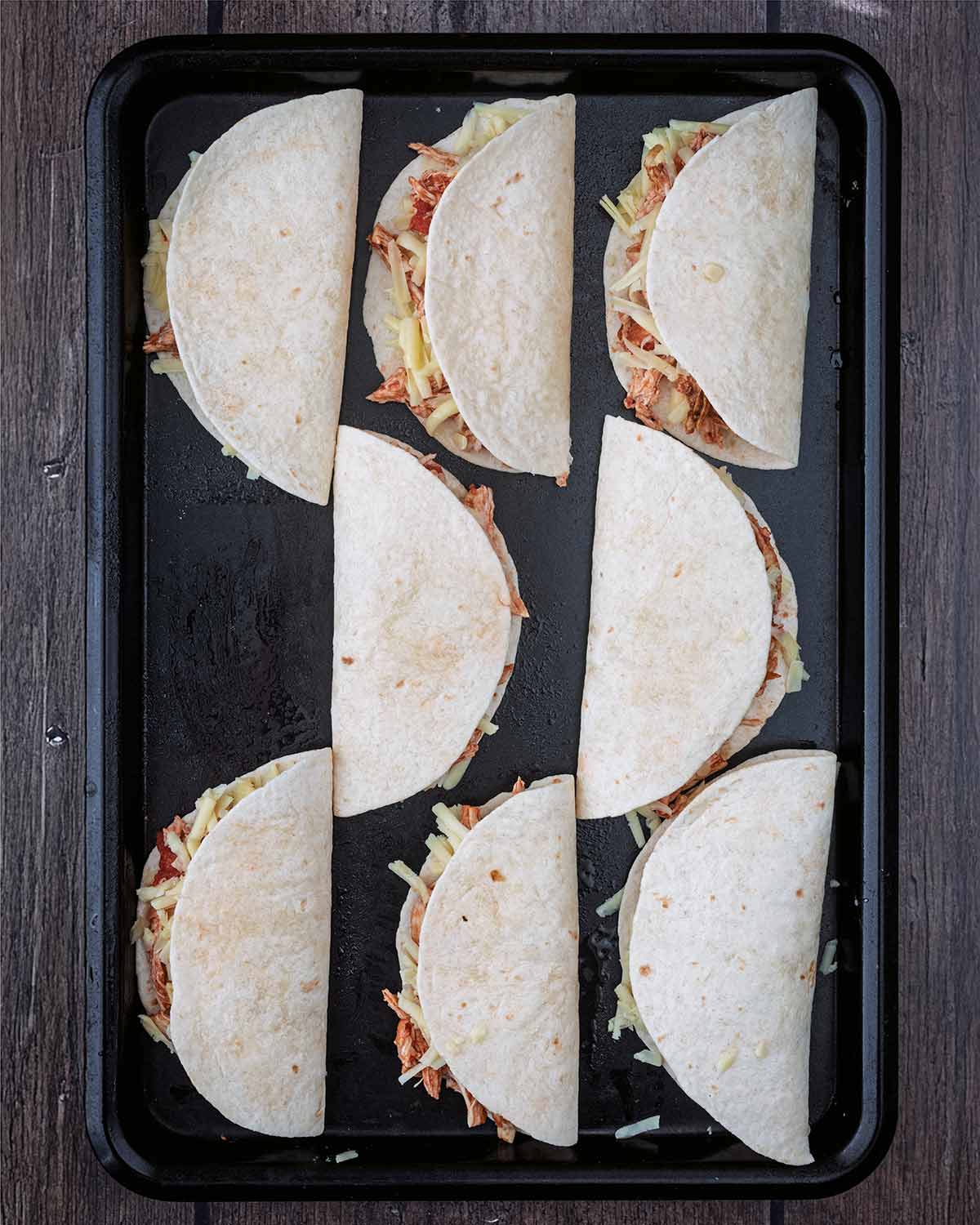 Eight folded tacos on a baking tray.