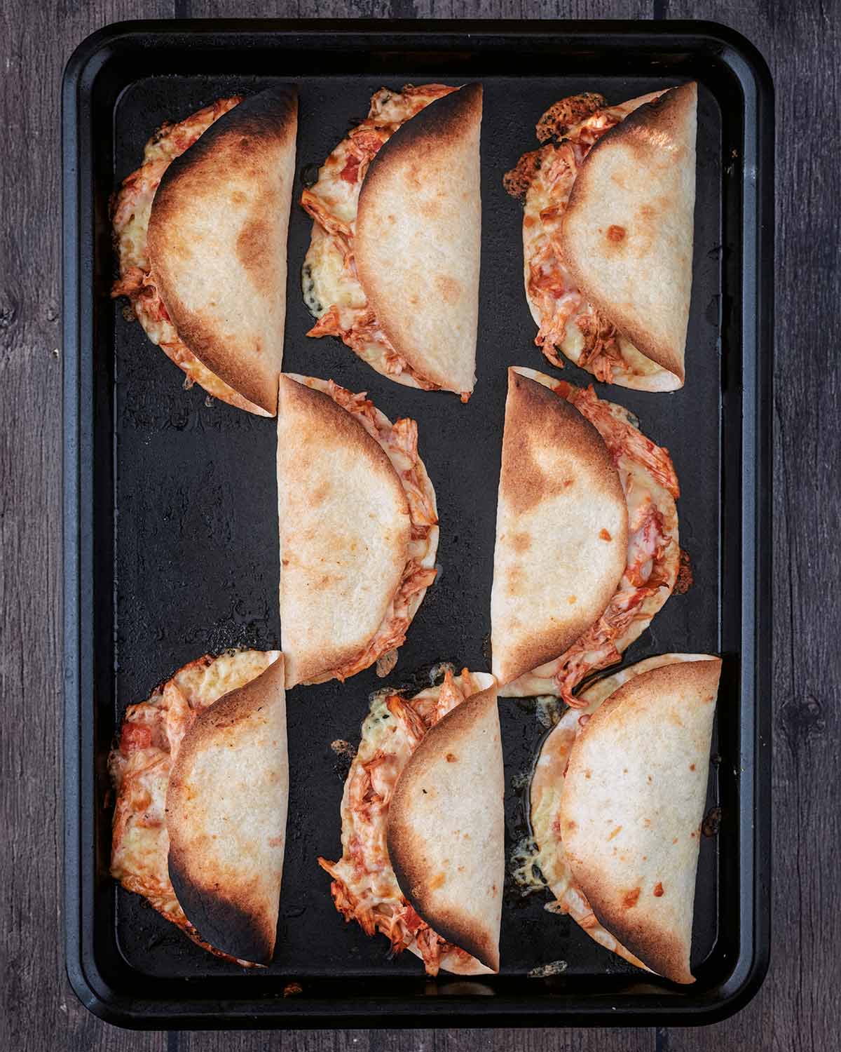 Eight baked tortillas on a baking tray.