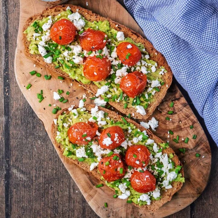 Two slices of tomato avocado toast on a wooden serving board.