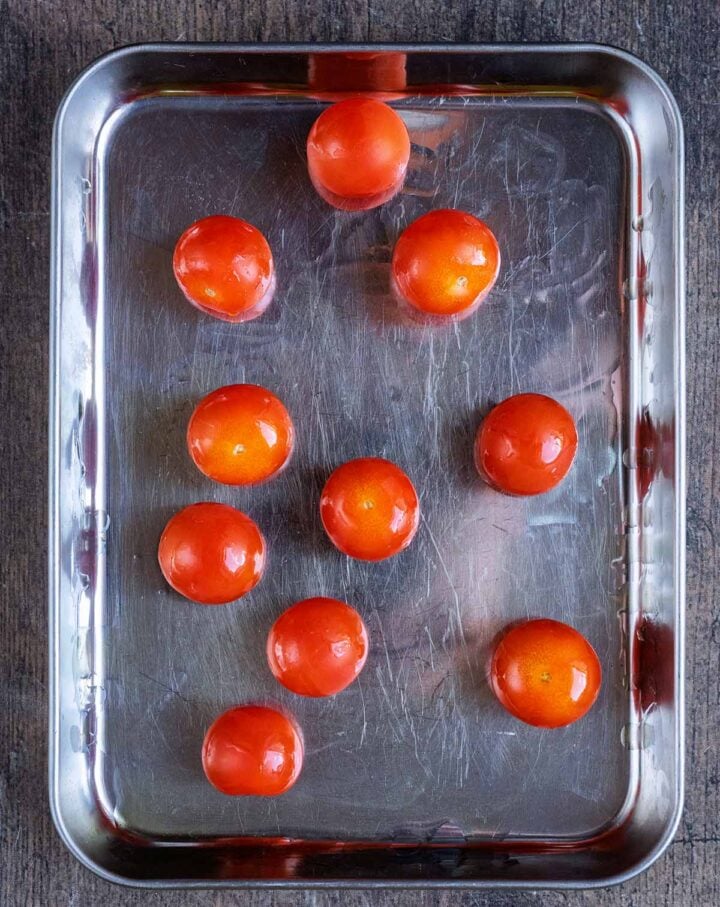 Ten whole cherry tomatoes drizzled with oil, on a baking tray.