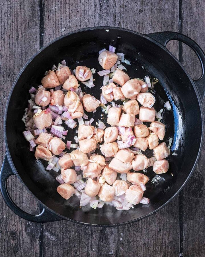 Slices of sausage and chopped onion cooking in a large black pan.
