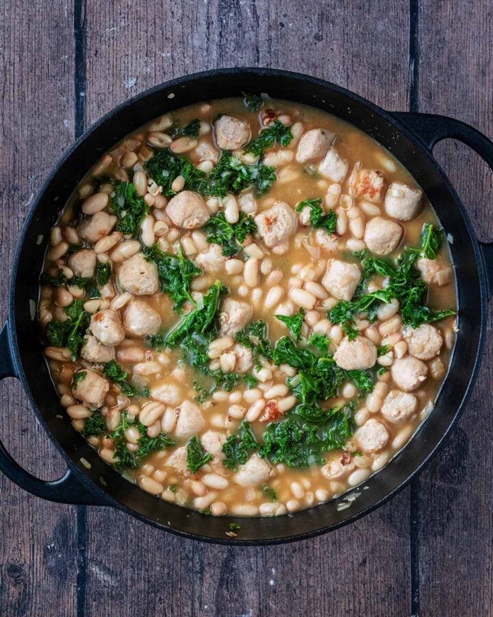 Cooked beans, sausage and kale in the black pan.