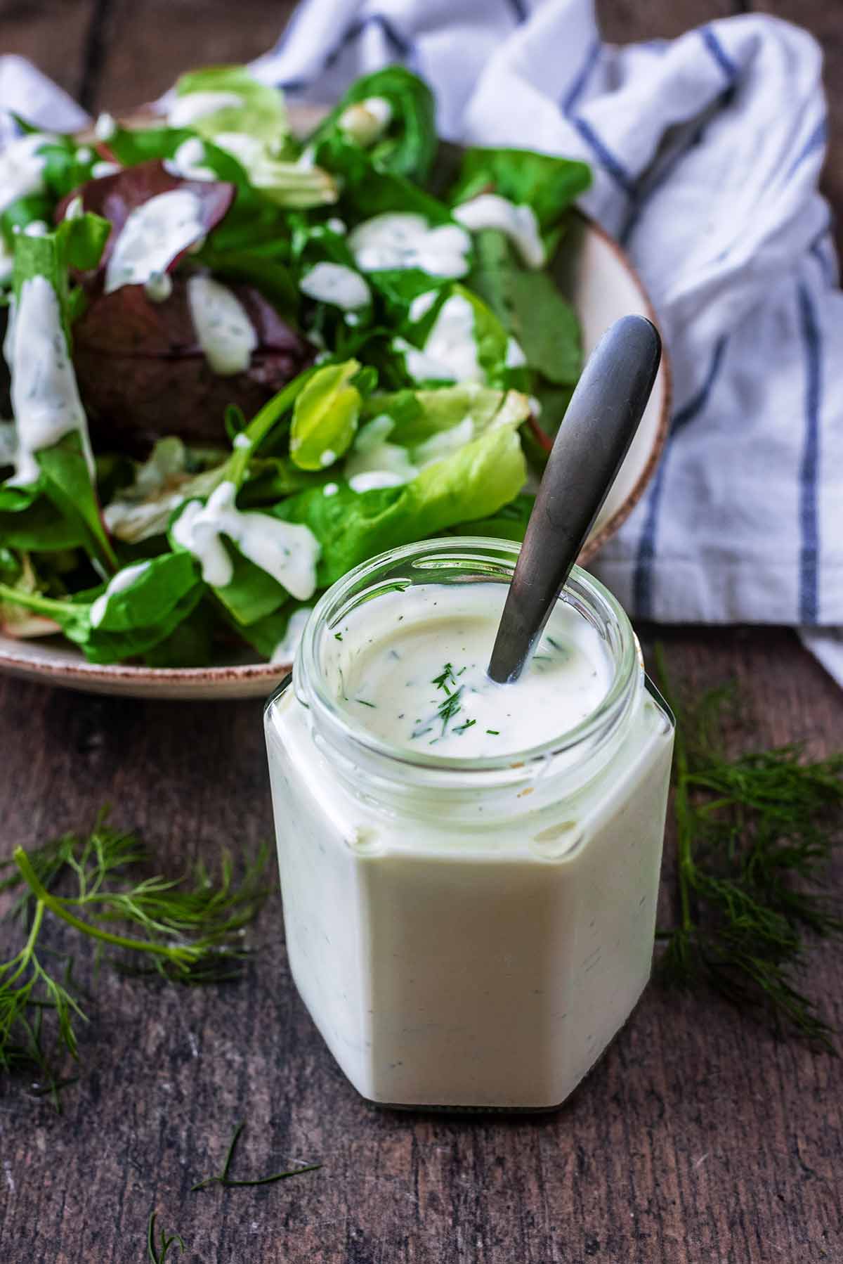 A jar of creamy salad dressing in front of a bowl of salad.