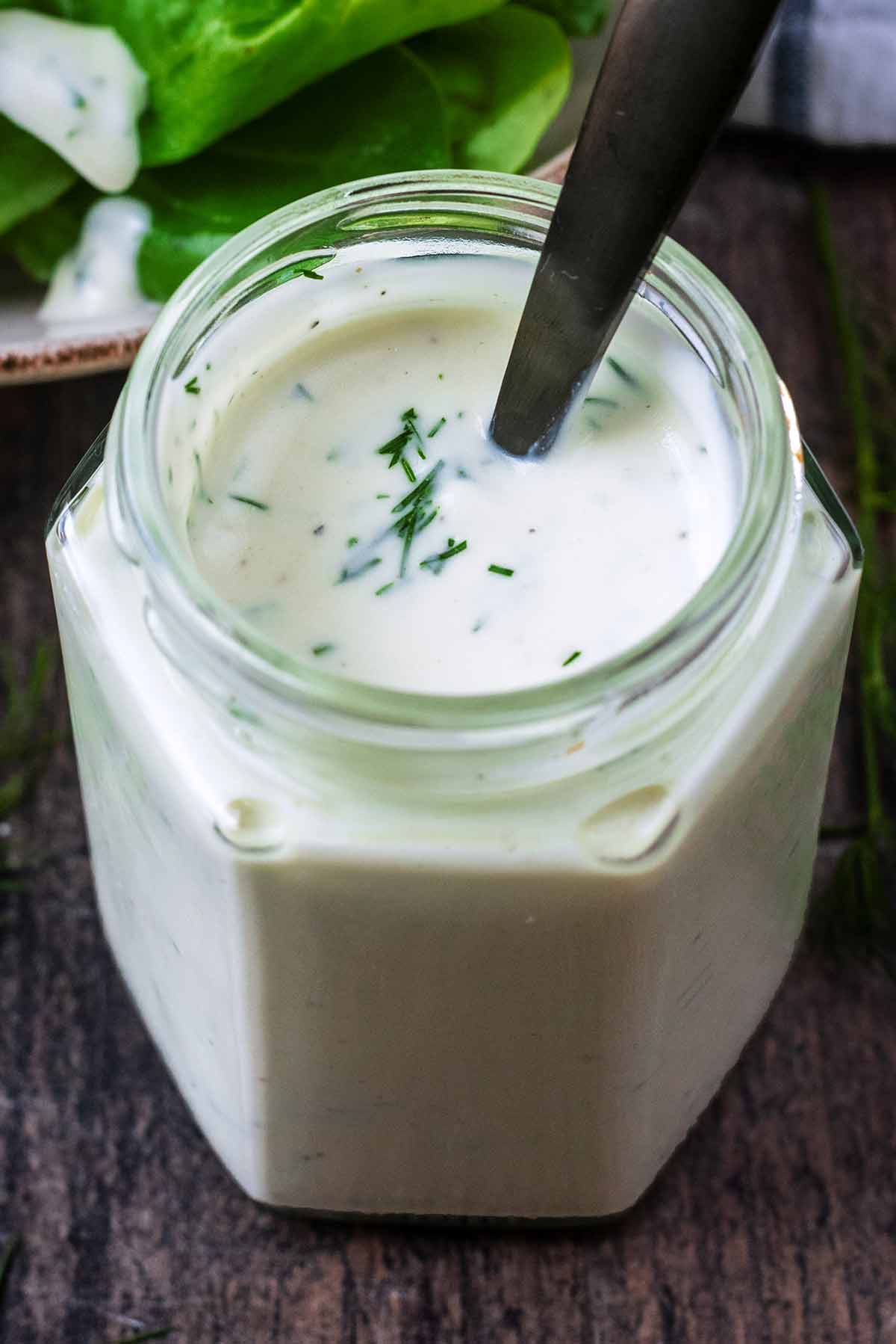 A jar of creamy yogurt based salad dressing with a small black spoon in it.