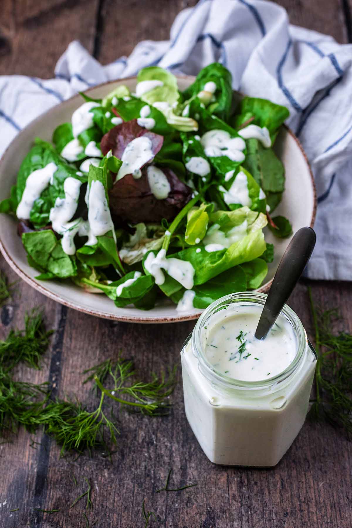 A bowl of salad leaves dressed in a creamy dressing with a jar of dressing in the foreground.