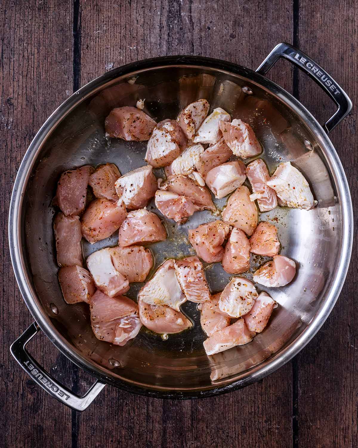 Chunks of chicken breast cooking in a large silver pan.
