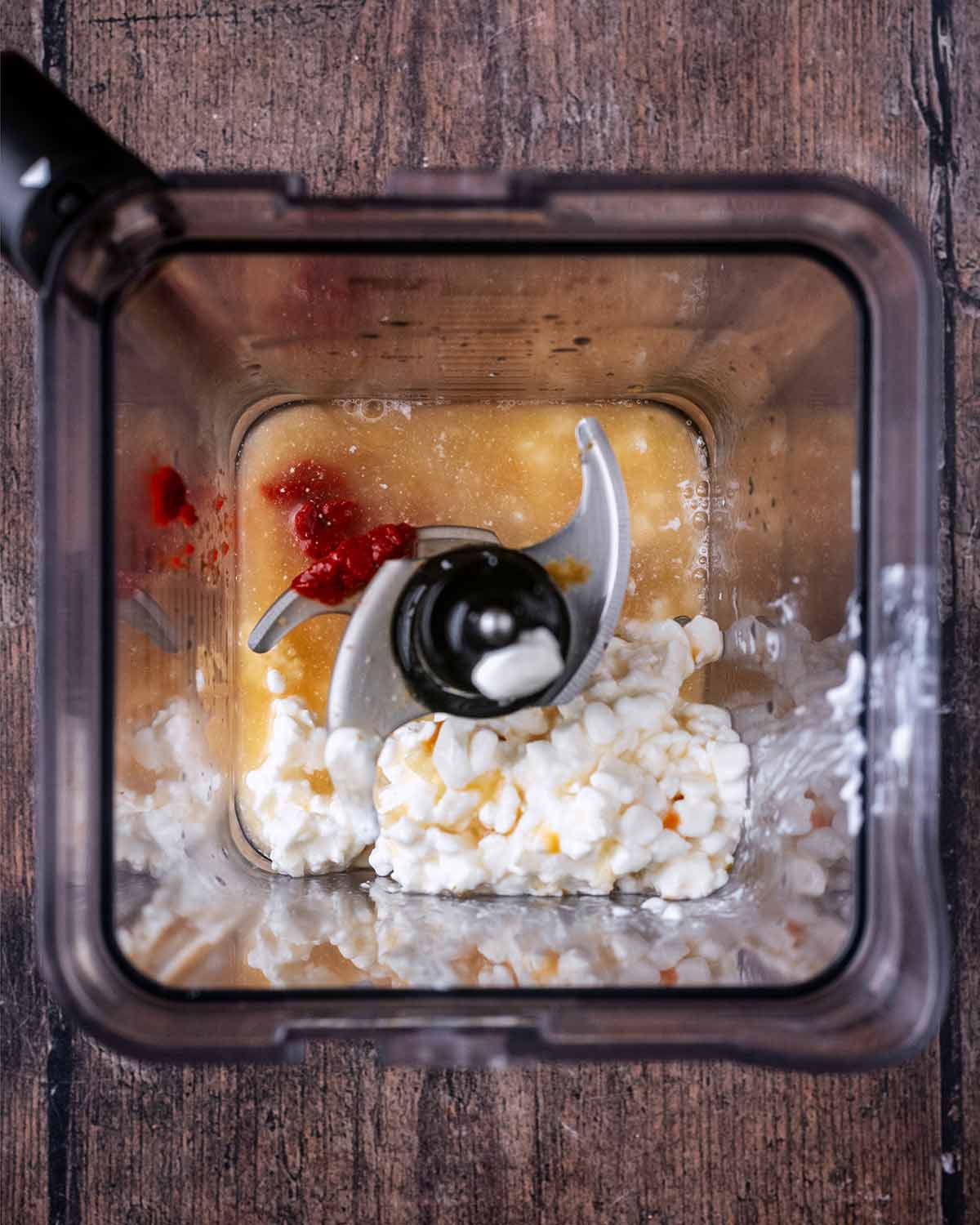 A blender jug containing stock, cottage cheese, garlic and tomato purree.