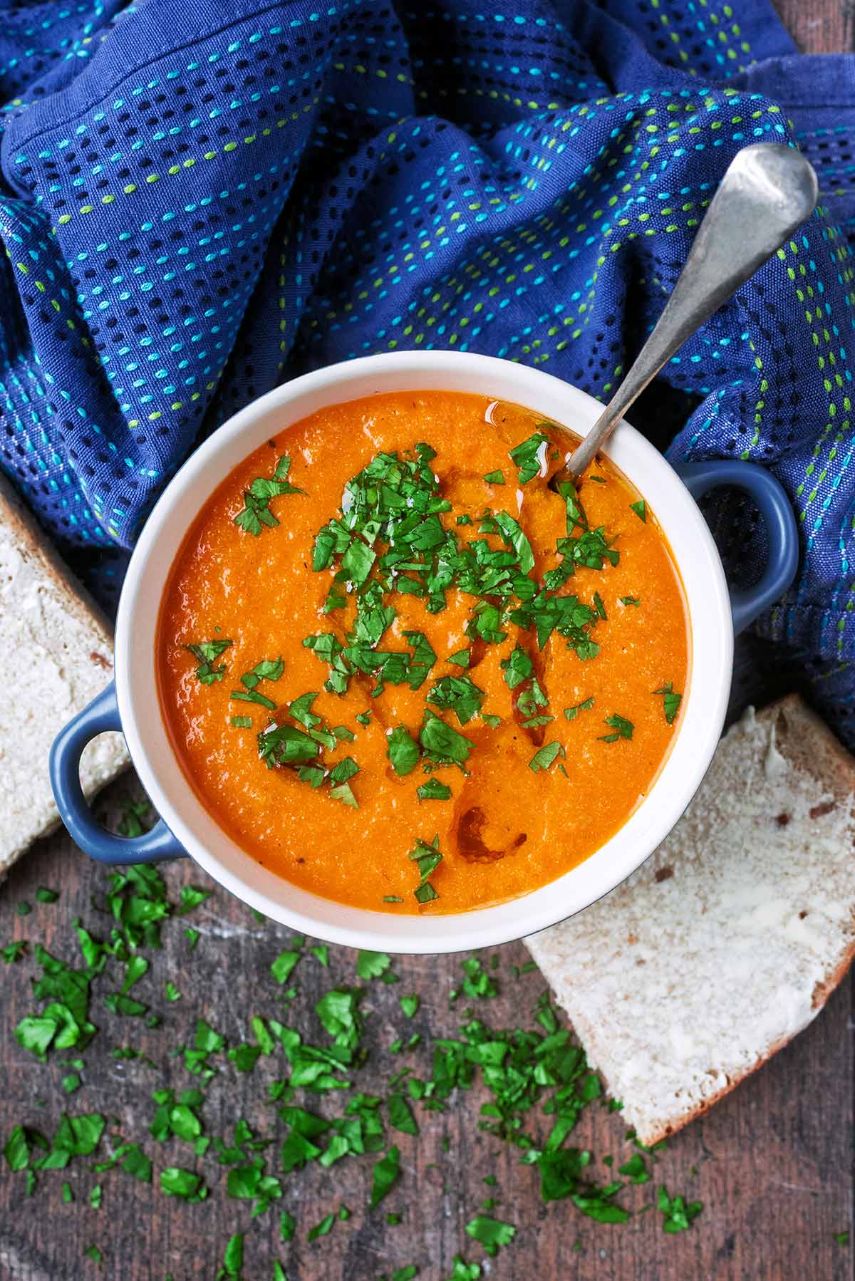 A bowl of tomato soup with a spoon in it next to a blue towel.