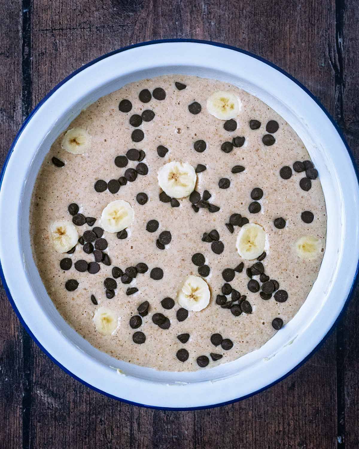 Banana bread batter in a baking dish with chocolate chips and banana sices.
