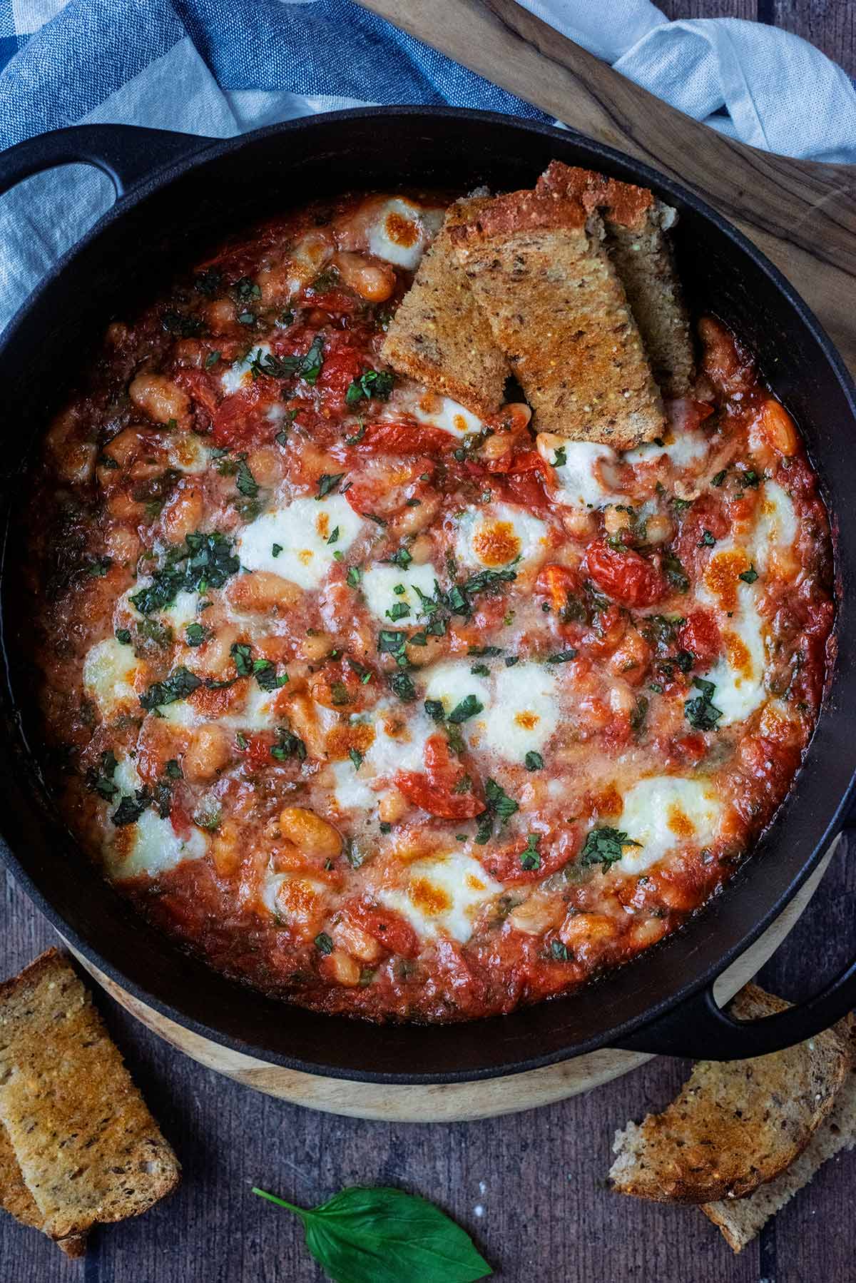 Cooked beans in a cheesy tomato sauce in a large black pan.