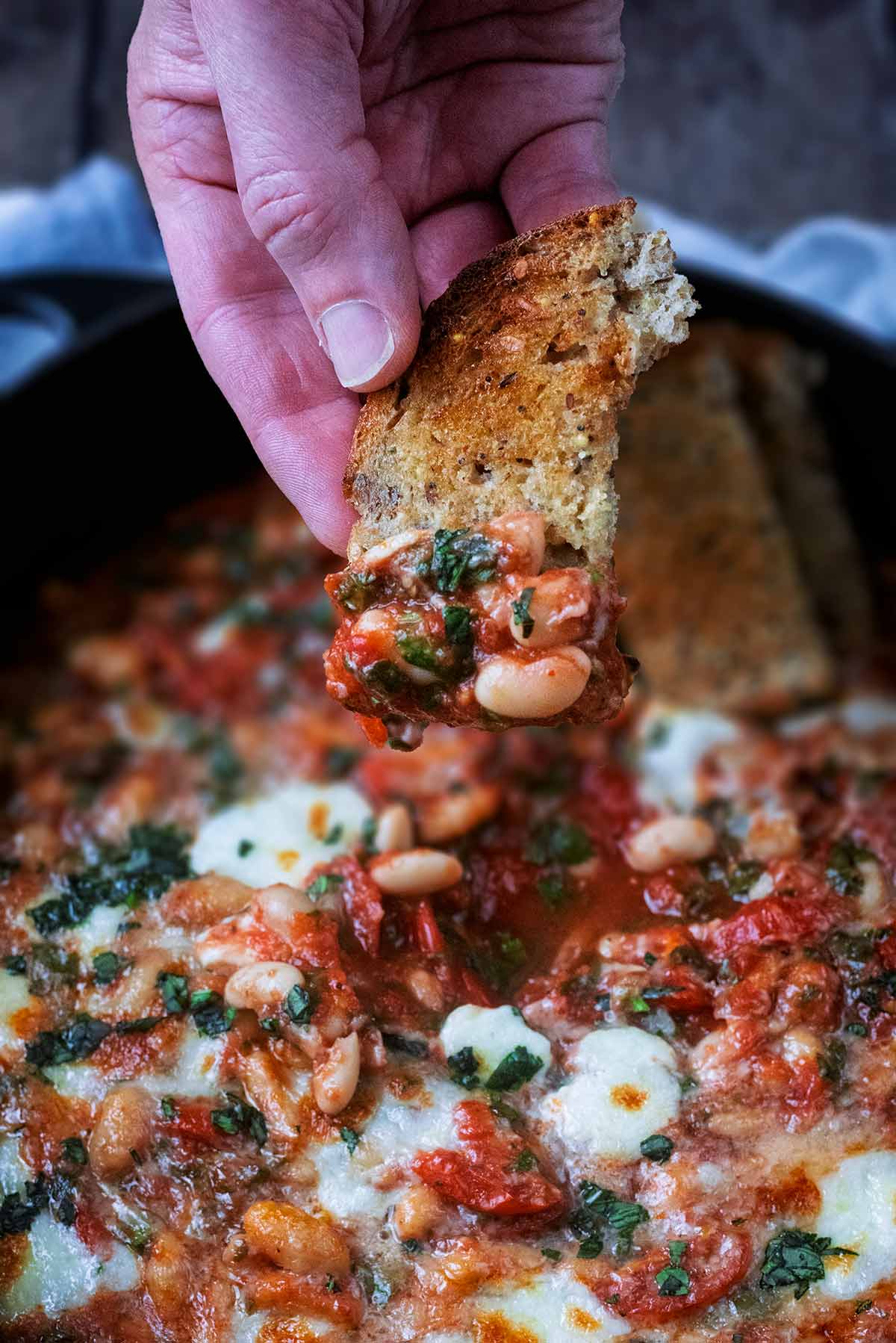 A hand holding a piece of toasted bread scooping up some beans.