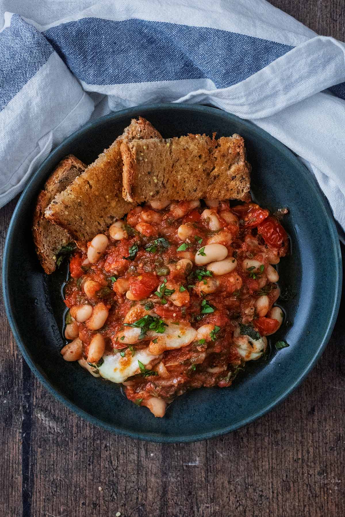 A plate of cheesy beans with some small sliced of toasted bread.