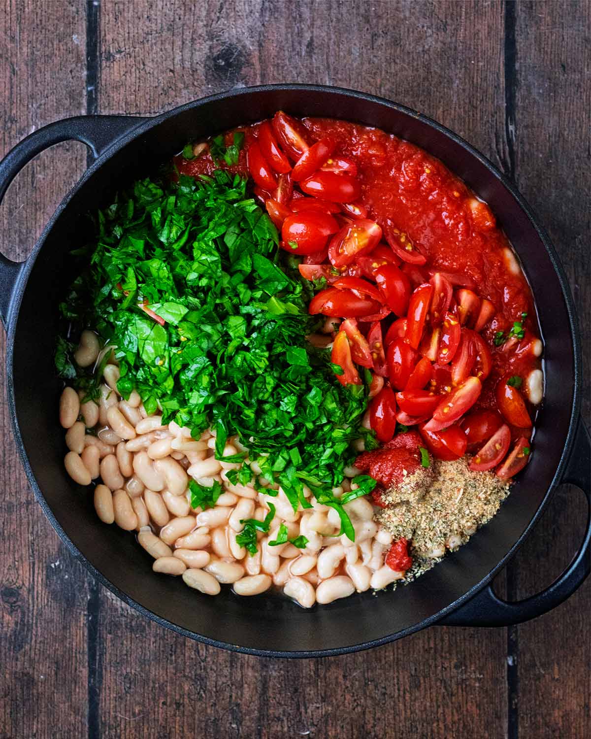 A large pan containing white beans, tomatoes, spinach and seasoning.