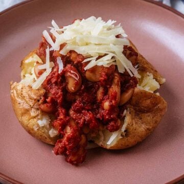 Jacket potato with cheese and beans on a pink plate.