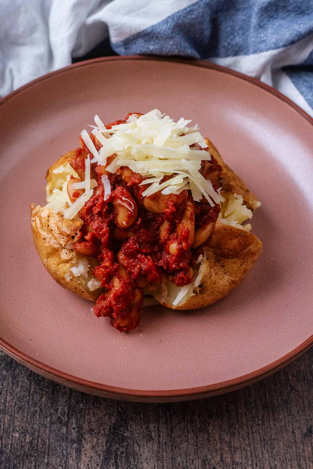 A baked potato topped with baked beans and grated cheese.