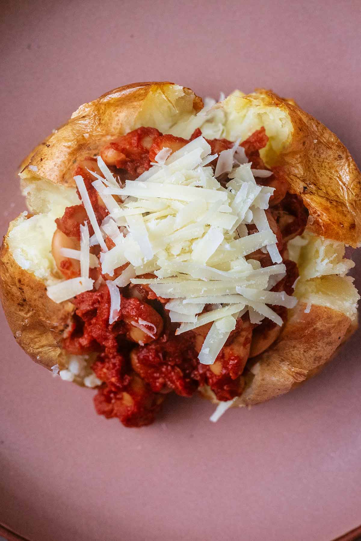 Grated cheese and homemade baked beans on top of a jacket potato.