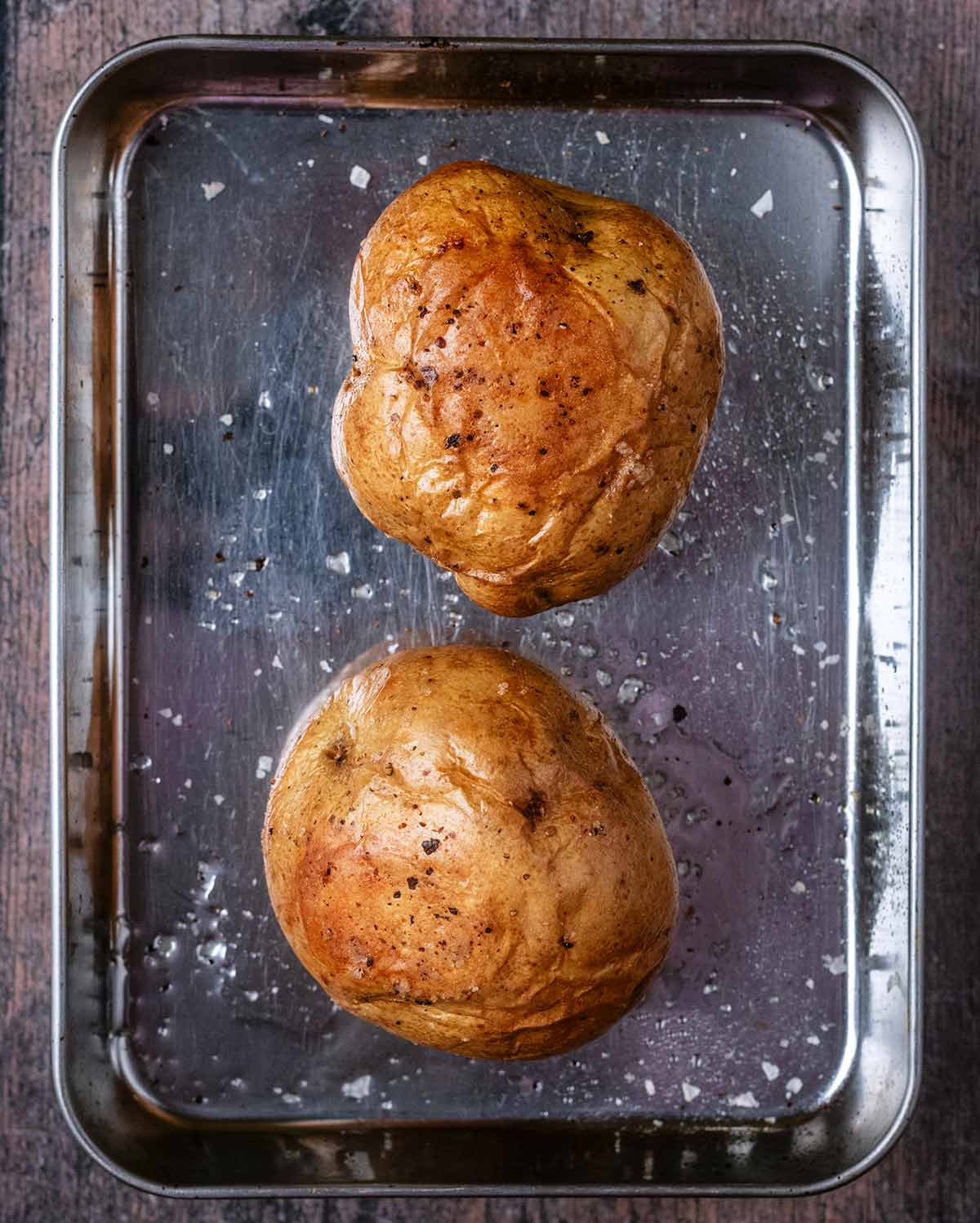 Two cooked baked potatoes on a baking tray.