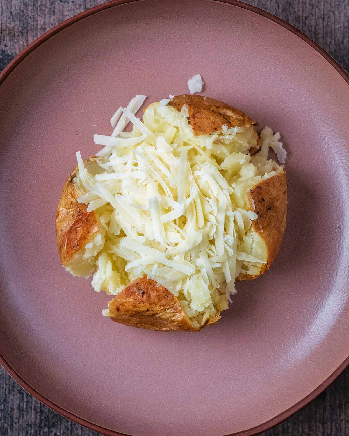 A baked potato with grated cheese on top of it.