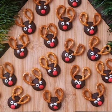 Seventeen chocolate button reindeers on a wooden board.