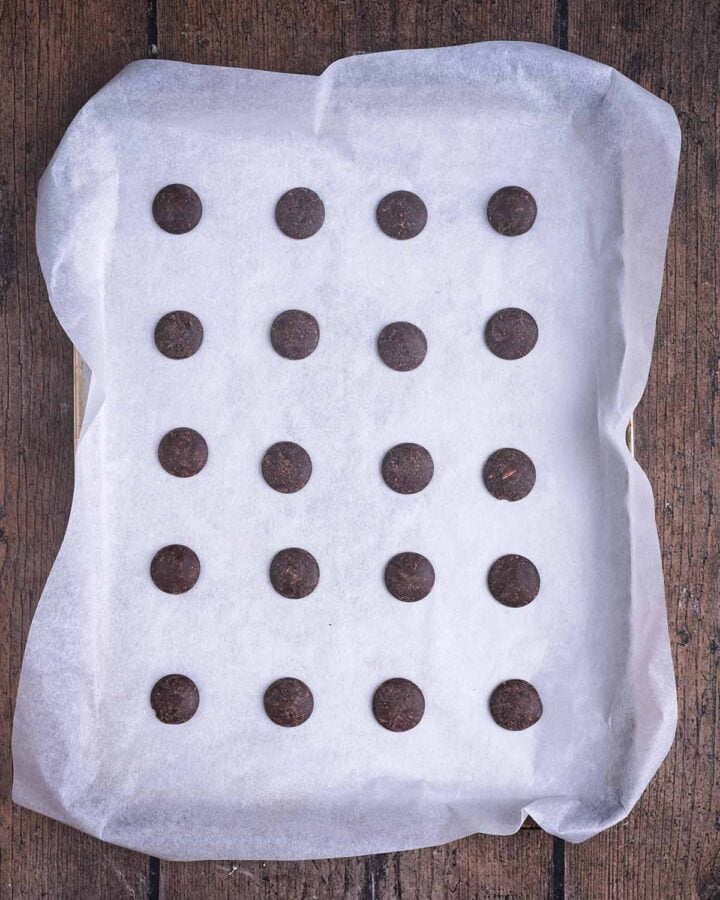 Twenty chocolate buttons on a lined baking tray.