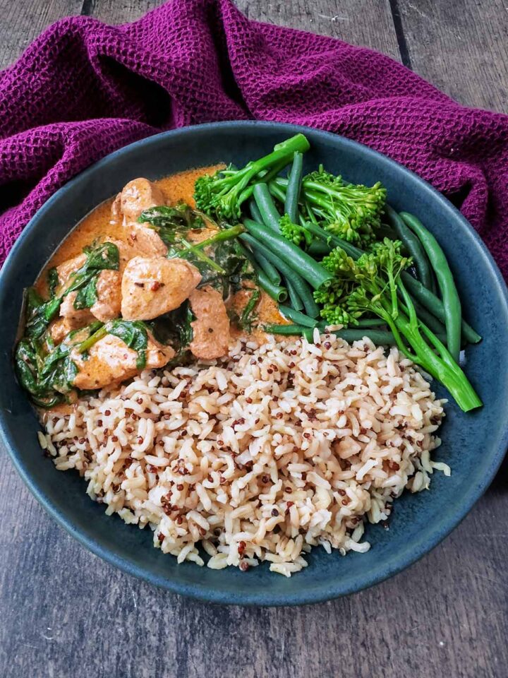 A bowl of Thai red curry, rice and broccoli in front of a purple towel.