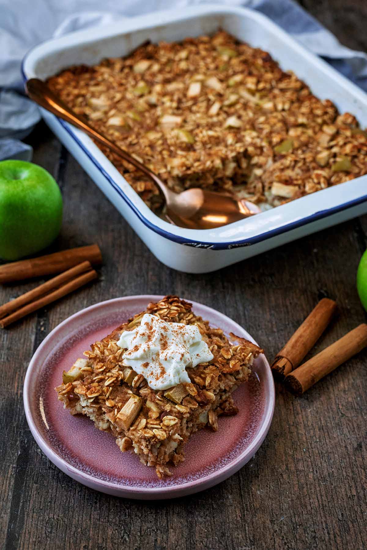 A portion of baked oats on a plate in front of a pan of more oats.