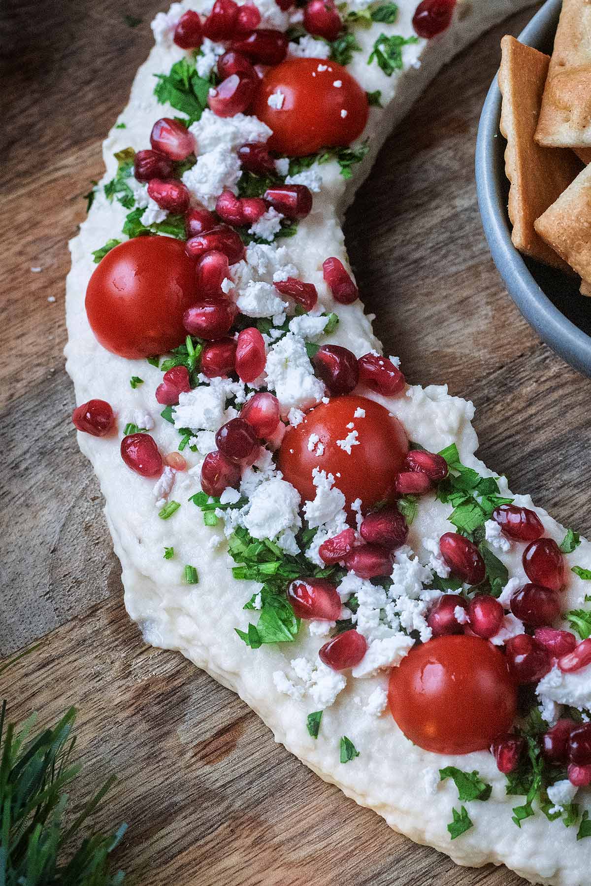 Halved tomatoes, pomegranate seeds, feta cheese and herbs on top of some hummus.