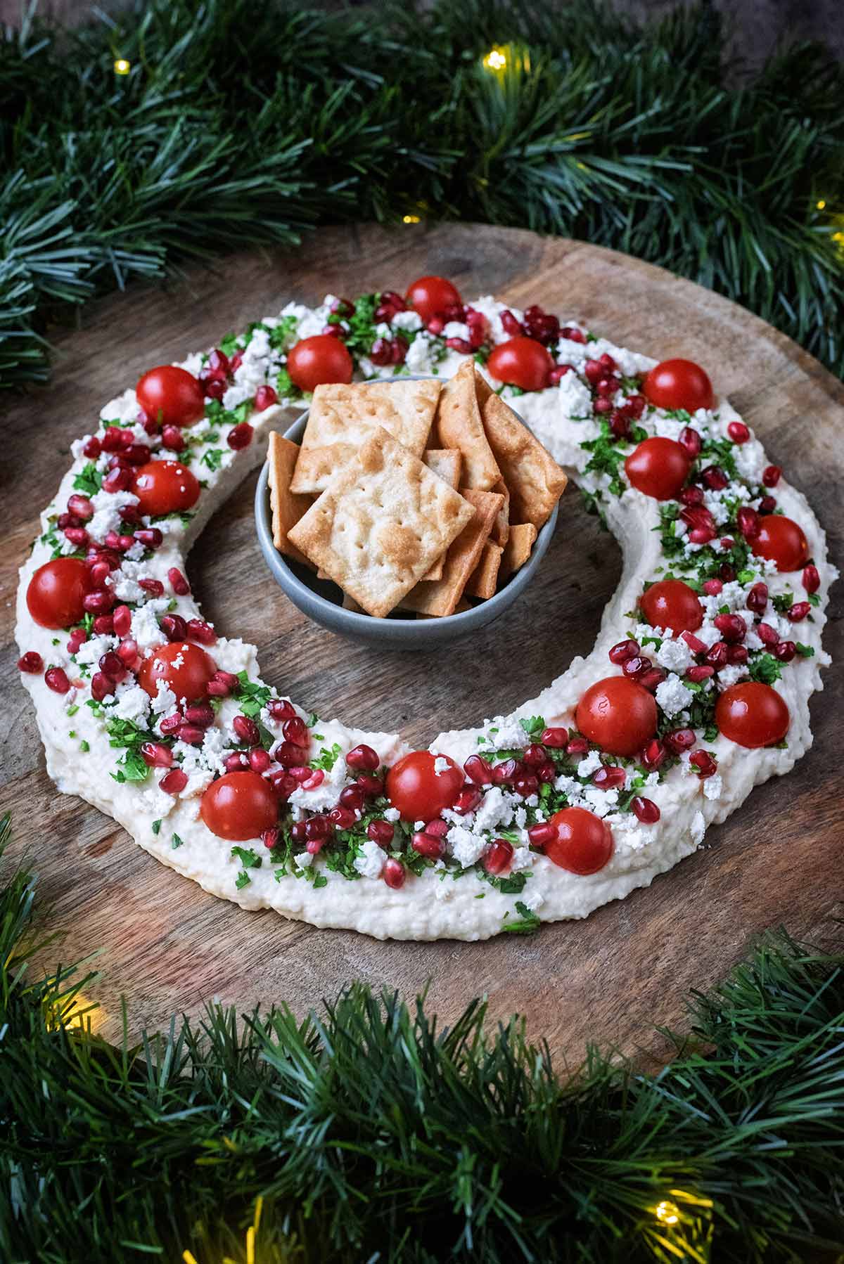 A bowl of square crackers in the middle of a ring of hummus.
