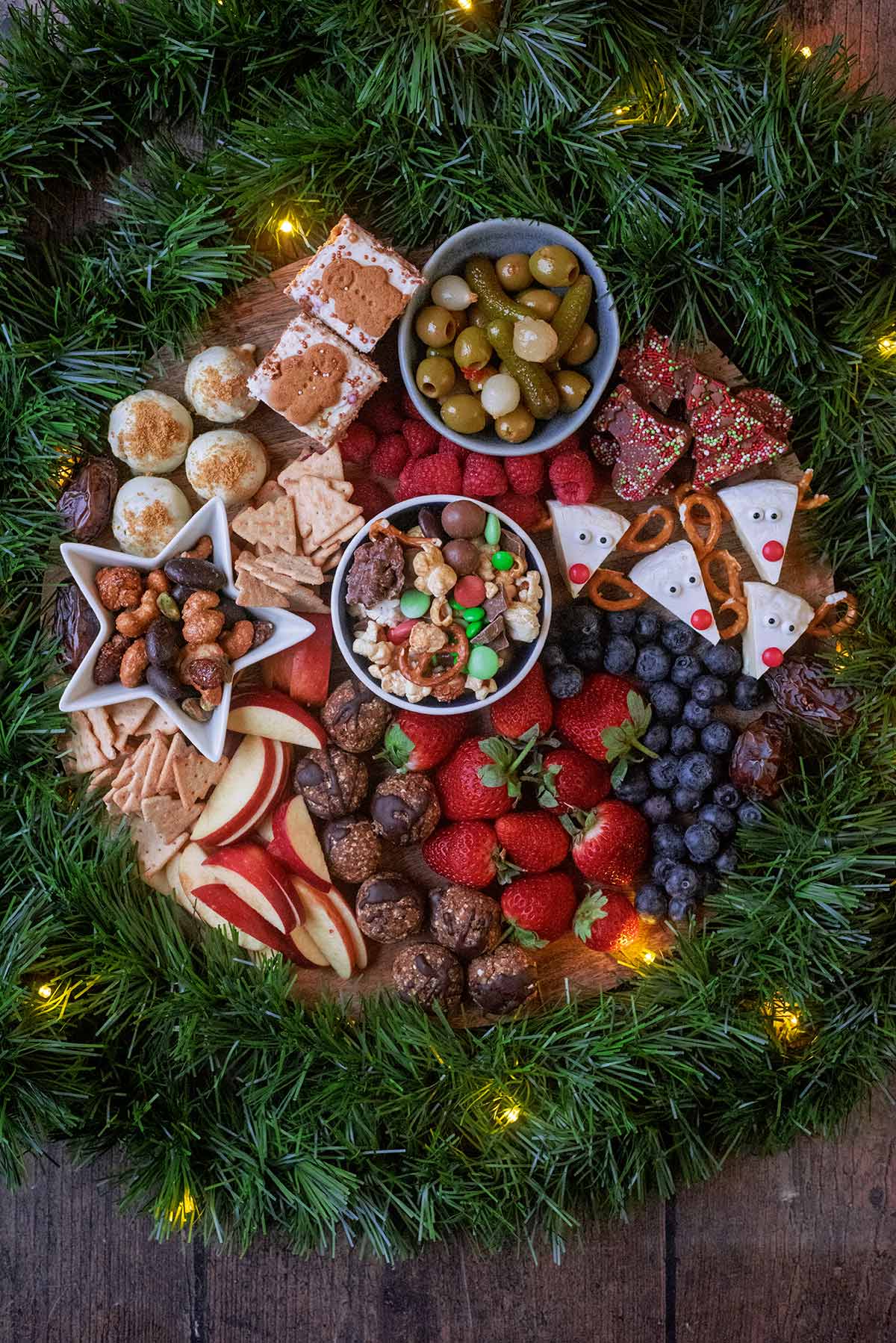 A Christmas themed snack board surrounded by green garland and fairy lights.
