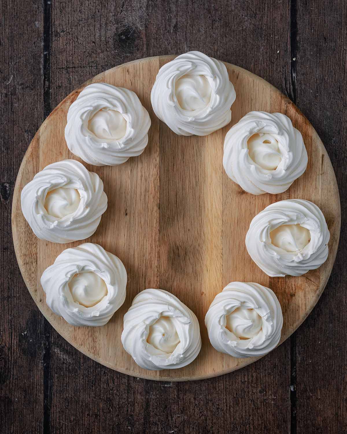 Eight mini meringue nests arranged in a circle on wooden board.