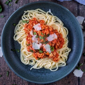 A bowl of chicken bolognese on a bes of cooked spaghetti.