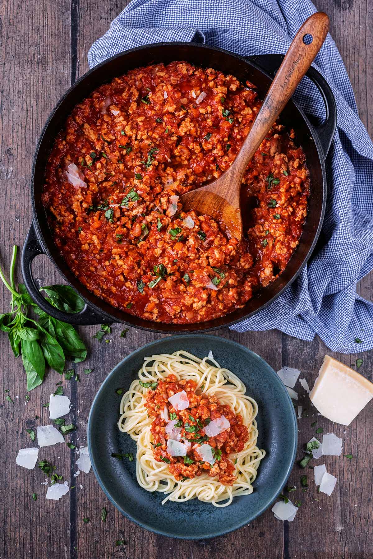 A large pan of bolognese next to a plate with a portion of spaghetti and bolognese.