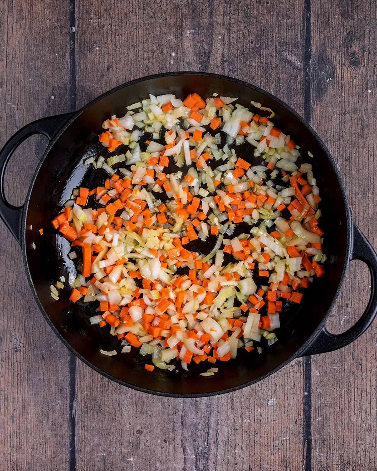 Diced onion and carrot cooking in a large black pan.